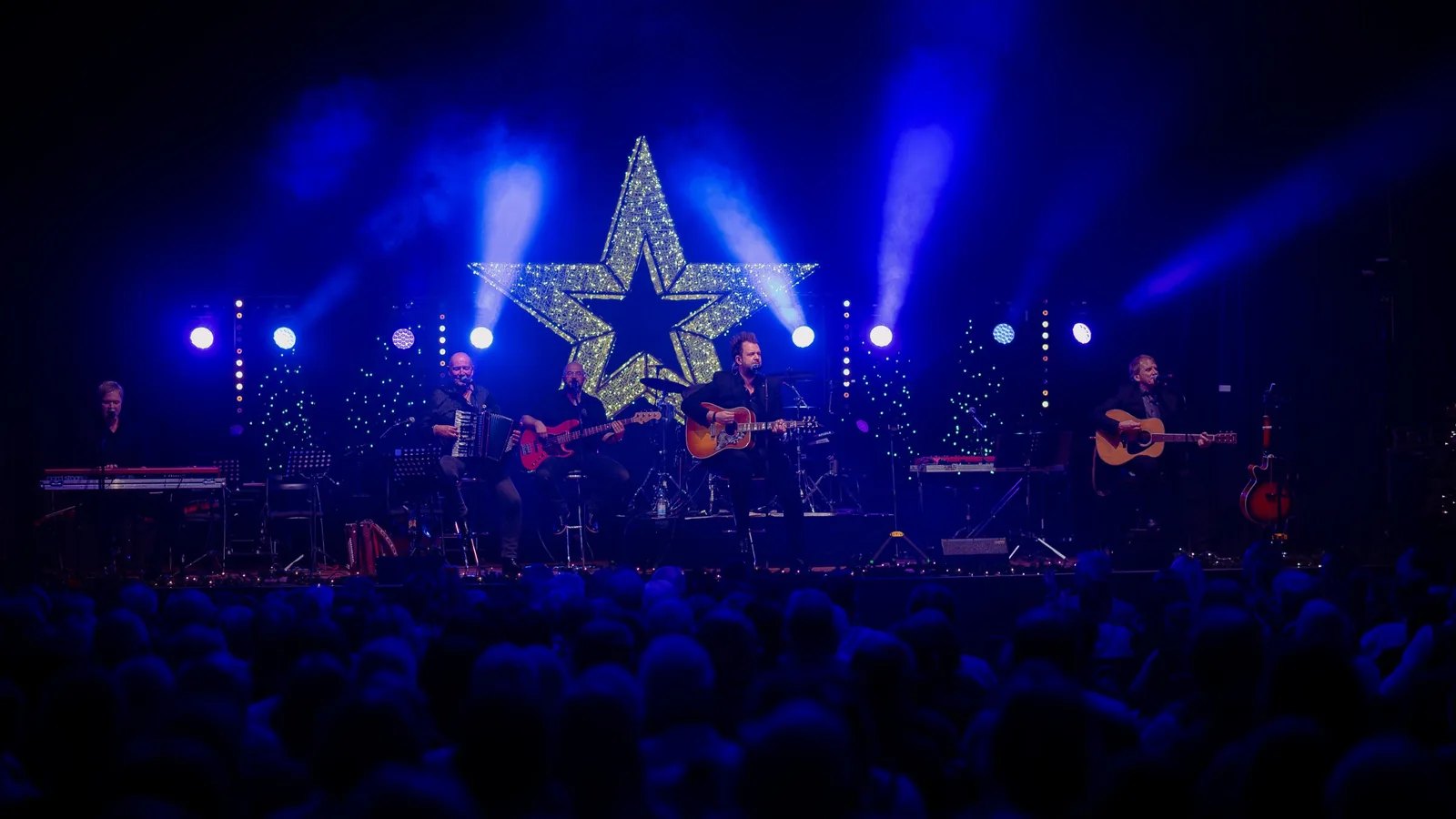 Konzertfilm Paveier Kölsche Weihnacht: Band auf der Bühne unter einem leuchtenden Stern, davor das Publikum